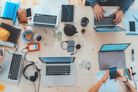 A group of work laptops that have been set up on a large work desk.